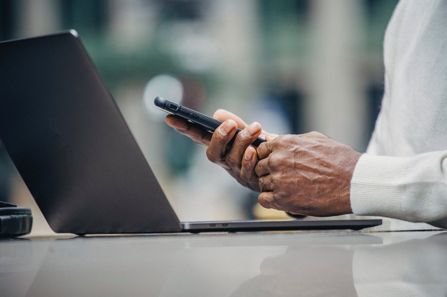crop ethnic man using smartphone while working on netbook in outdoor cafe